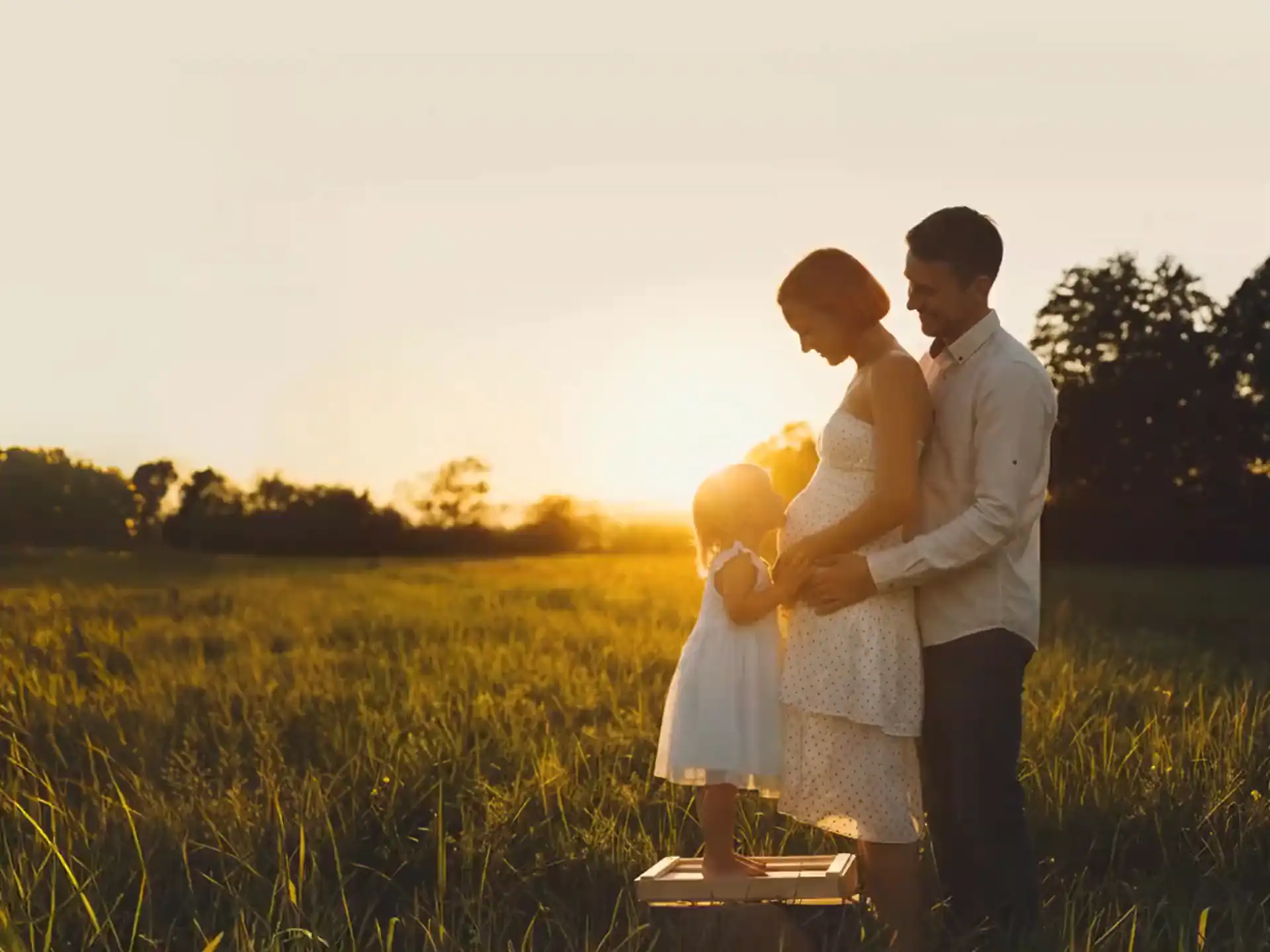 A family in a sunlit field at golden hour, expecting a new child